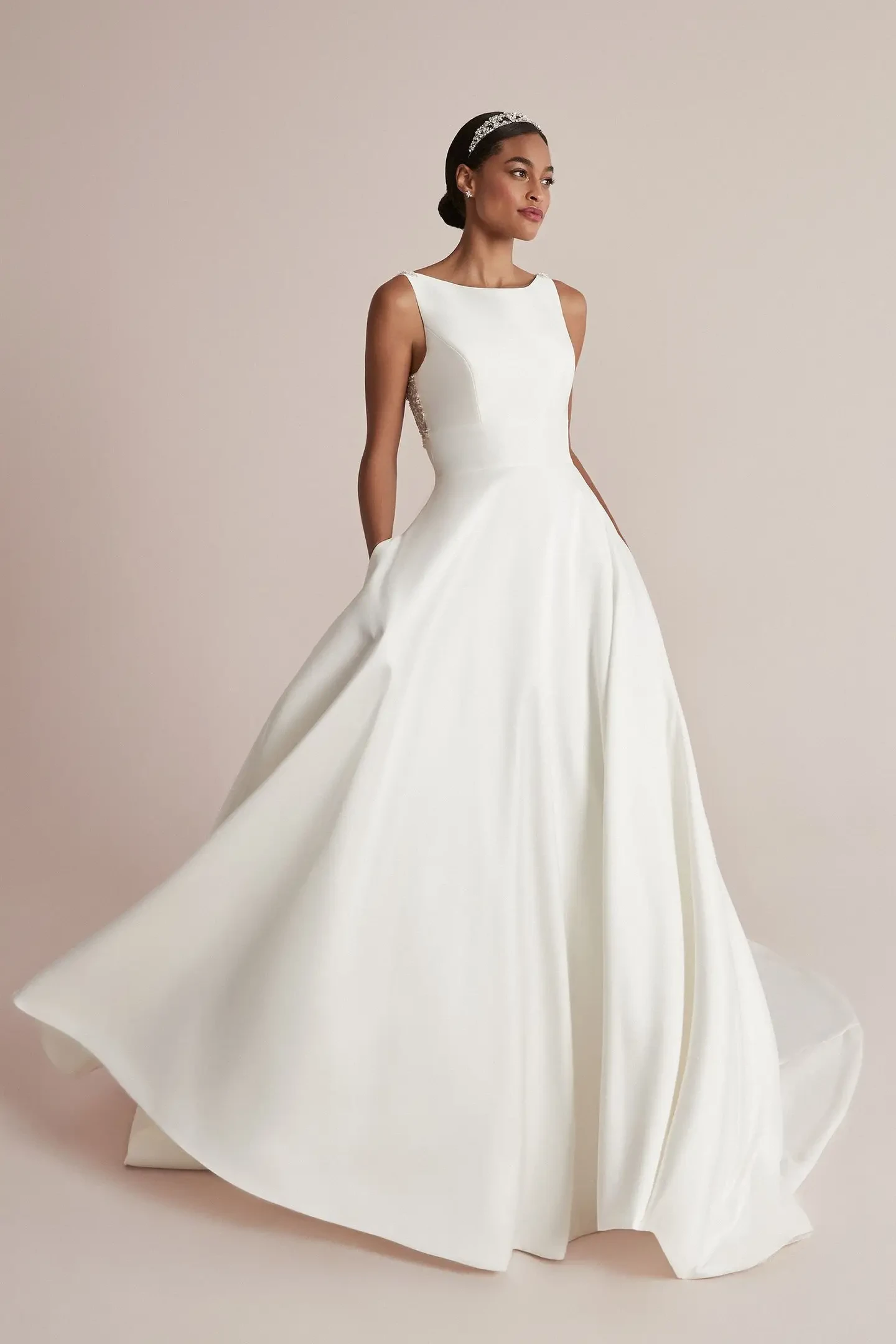 A model wearing an elegant, sleeveless white wedding dress with a flowing skirt, standing gracefully against a neutral background.
