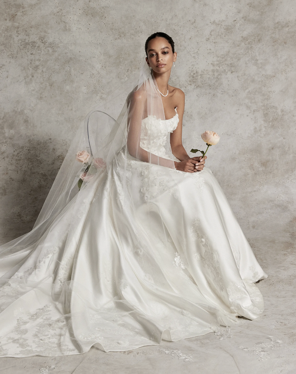 Bride in a veil holding a rose, seated in a wedding gown