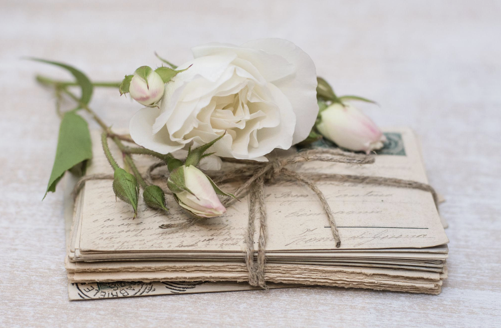 White rose resting on a bundle of handwritten letters tied with twine